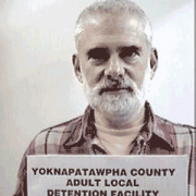 Older man with white hair, mustache and beard holding a jail booking card